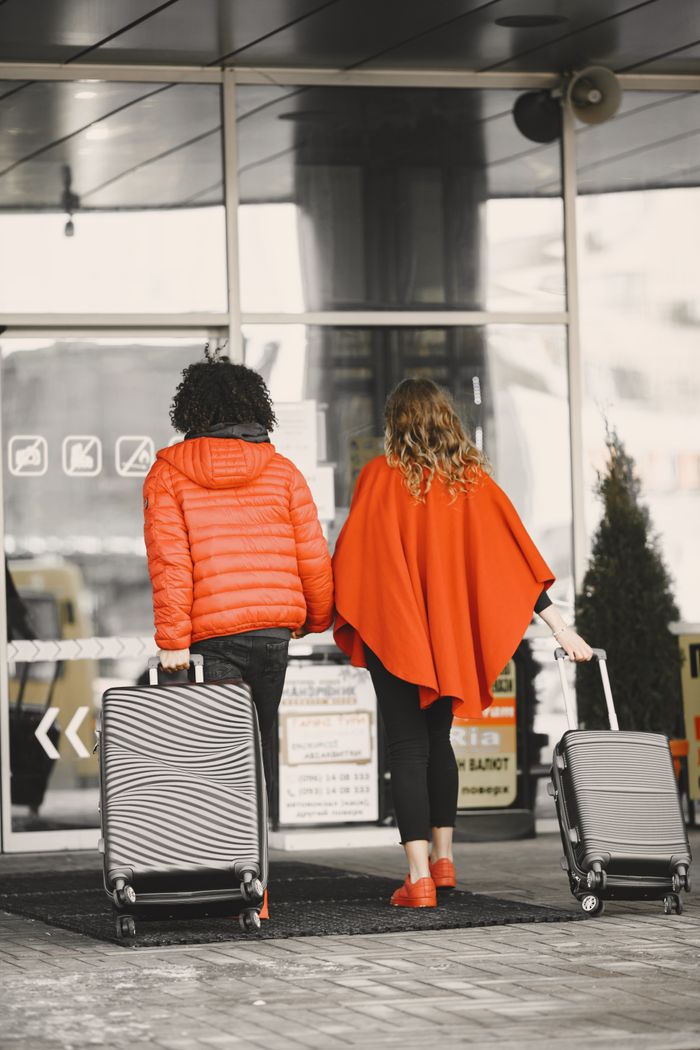 about-us-01 Back view of a couple in bright clothing entering an airport with suitcases.