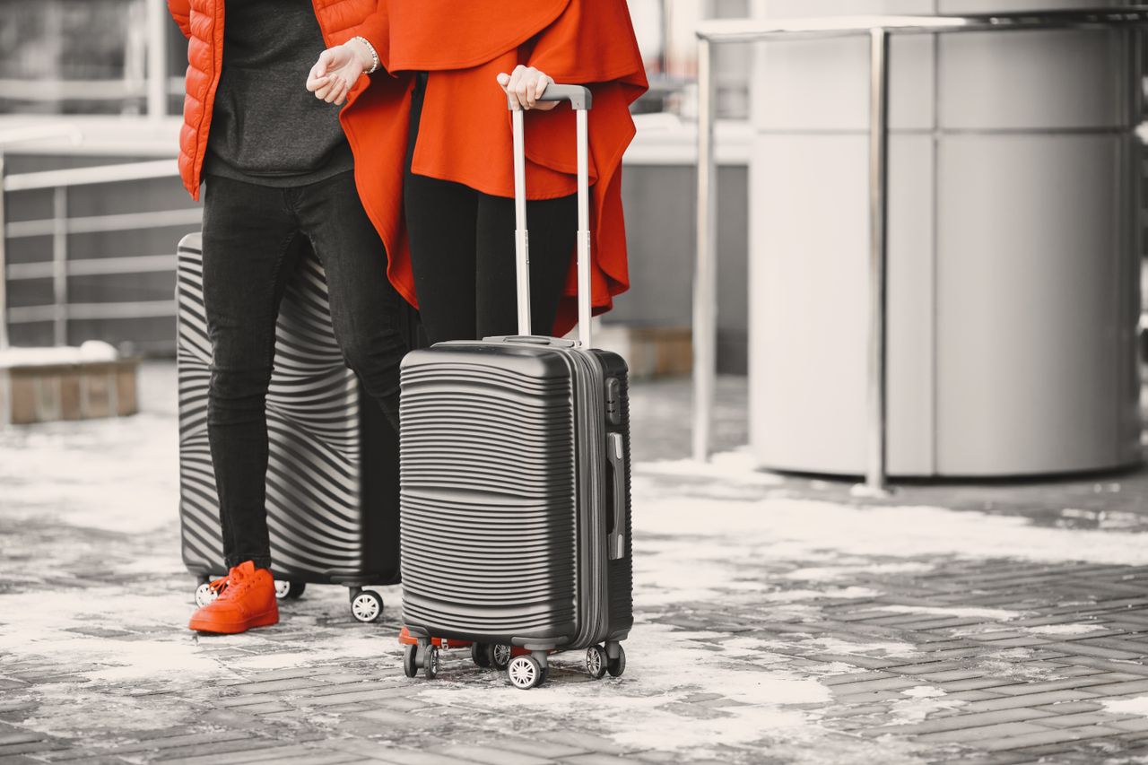 heros-img A fashionable couple in winter attire with sleek luggage, standing outdoors on a snowy day.
